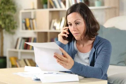 woman talking on phone looking over roof warranty papers
