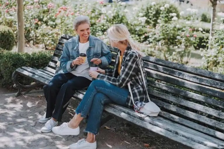 Two female friends with coffee sitting on a wooden bench at parks in clinton