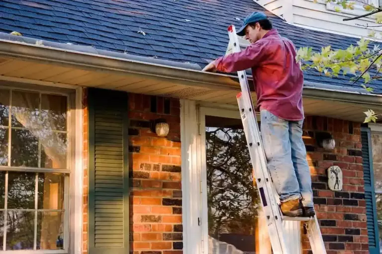 Man Cleaning Gutters on Ladder during roof maintenance