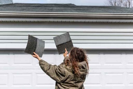female homeowner holding two cheap roof tile shingles inspecting roof scams