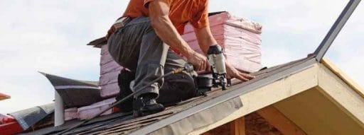 man fixing shingles on roof; roof warranty